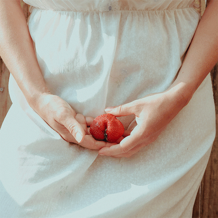 Pregnant person holding a strawberry over their belly.